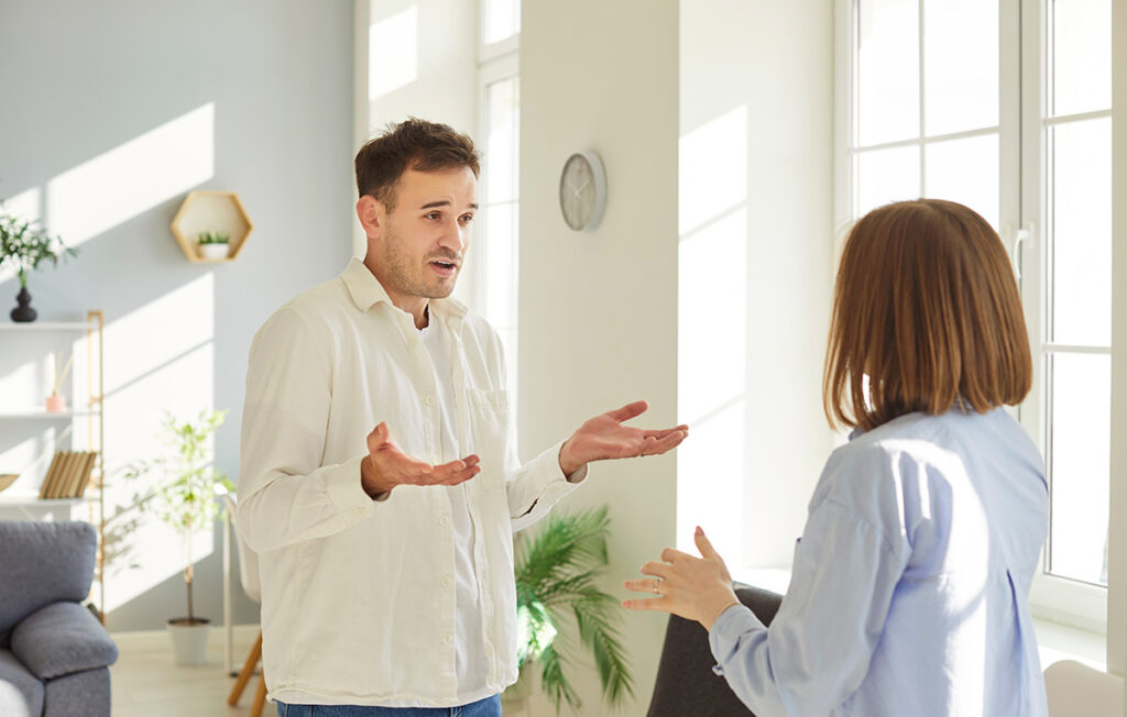 Frustrated young couple arguing with each other by window and struggling with relationship issues.
